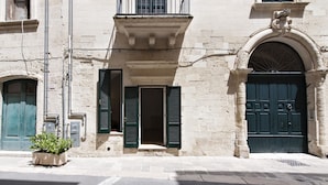 Un edificio con una amplia entrada en arco, un balcón con columnas y una puerta de color verde oscuro.