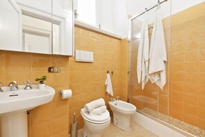 Ein Badezimmer mit Waschbecken, Toilette, Bidet und einer Duschkabine aus Glas.