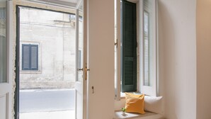 Una habitación con asiento junto a la ventana, una puerta y vista a la calle.
