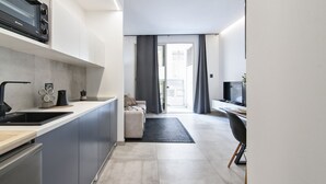Una cocina moderna con horno empotrado, cafetera y lavabo. Hay una zona de comedor con mesa y sillas, y vistas al exterior a través de una puerta corredera.