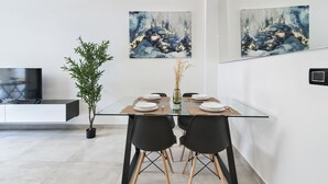 Un comedor moderno con una mesa de vidrio, sillas negras y dos cuadros abstractos en la pared.