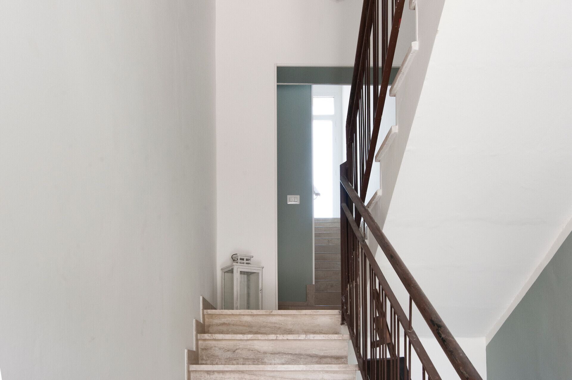 A staircase with a wooden handrail leading to a landing with a light switch.