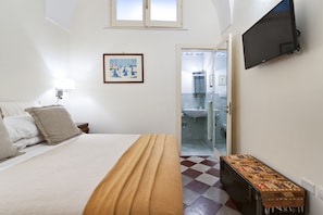Quarto com cama, mesa de cabeceira, televisão na parede e porta para o banheiro.