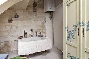 Um banheiro rústico com pia de pedra, banheira branca e porta de madeira com motivos florais azuis.