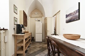 Uma cozinha estreita com uma mesa de madeira, cadeiras, uma máquina de café e uma geladeira.