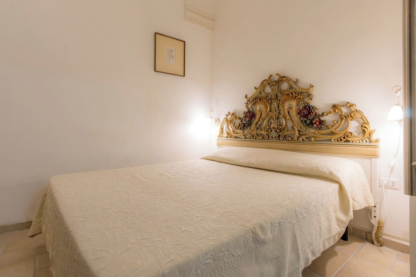 A bedroom with a large bed, ornate headboard, and a framed picture on the wall.