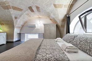 A bedroom with a stone ceiling, a bed with patterned bedding, a wardrobe, and a window with a view. - Arco Barocco - Lecce Selection (Lecce)
