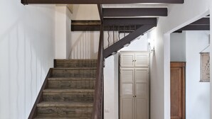 A wooden staircase with a dark metal handrail leading to a white door with louvered panels. - Arco Barocco - Lecce Selection (Lecce)