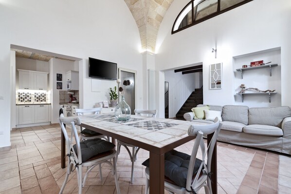 Un espacio habitable moderno con comedor, cocina y una escalera que sube a un altillo.