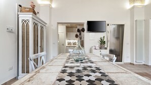 A dining area with a patterned floor, a central table with a vase, and a kitchen in the background. - Arco Barocco - Lecce Selection (Lecce)