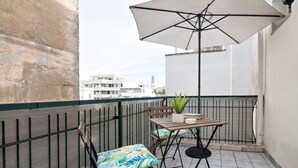 En balkon med et bord, stole, en potteplante og en stor parasol.