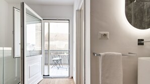 Et moderne badeværelse med et brusekabine i glas, et rundt spejl og et hvidt håndklæde på en håndklædestang.