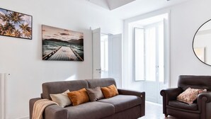 En moderne stue med en grå sofa, en brun lænestol og et stort vindue med havudsigt.