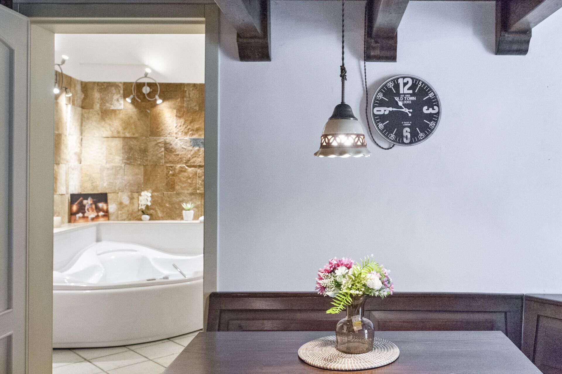 Un bagno con una vasca, una sveglia e un vaso con fiori su un tavolo.