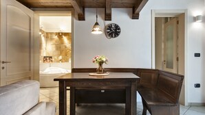 A dining area with a wooden table, bench seating, a wall clock, and a stone wall with a bathtub visible through an open door. - Baglivi 17 - Lecce Selection (Lecce)