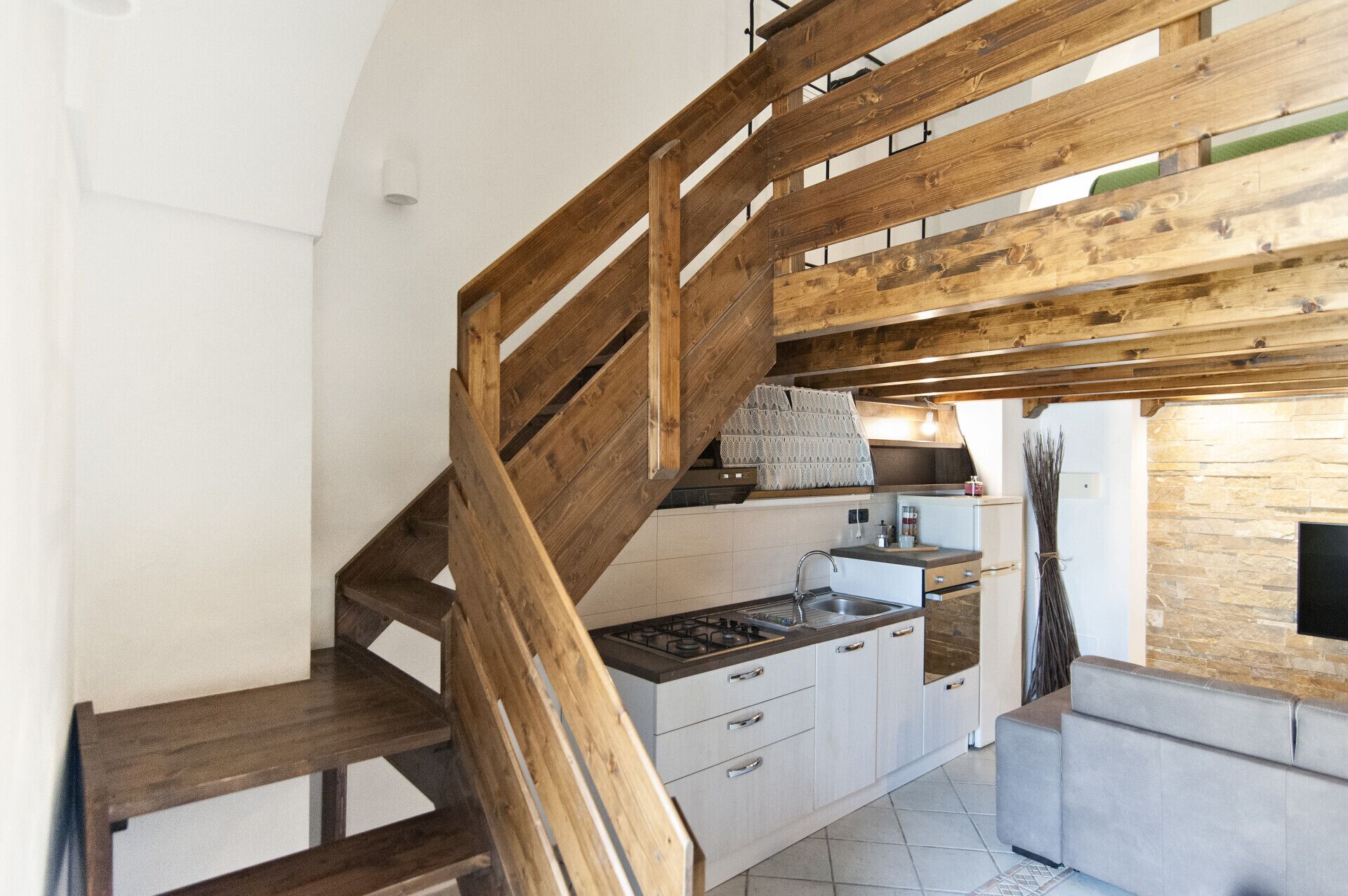Cucina con una scala in legno, un fornello a gas e un muro in pietra.