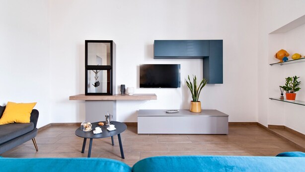 A modern living room with a grey sofa, a blue armchair, a coffee table with pastries, a TV, and a plant.