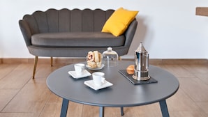 A modern room with a round table set for tea, a sofa with a yellow pillow, and a decorative metal object.