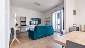 A modern living room with a blue sofa, a dining table, and a kitchen area in the background.