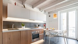 Cocina moderna con armarios de madera, horno empotrado y comedor con sillas blancas y una mesa.