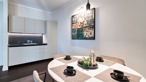 A modern kitchen with white cabinets and a black countertop, a dining table with four black cups and saucers, and a large abstract painting on the wall. - HON Lecce Hospitality - Lecce Selection (Lecce)