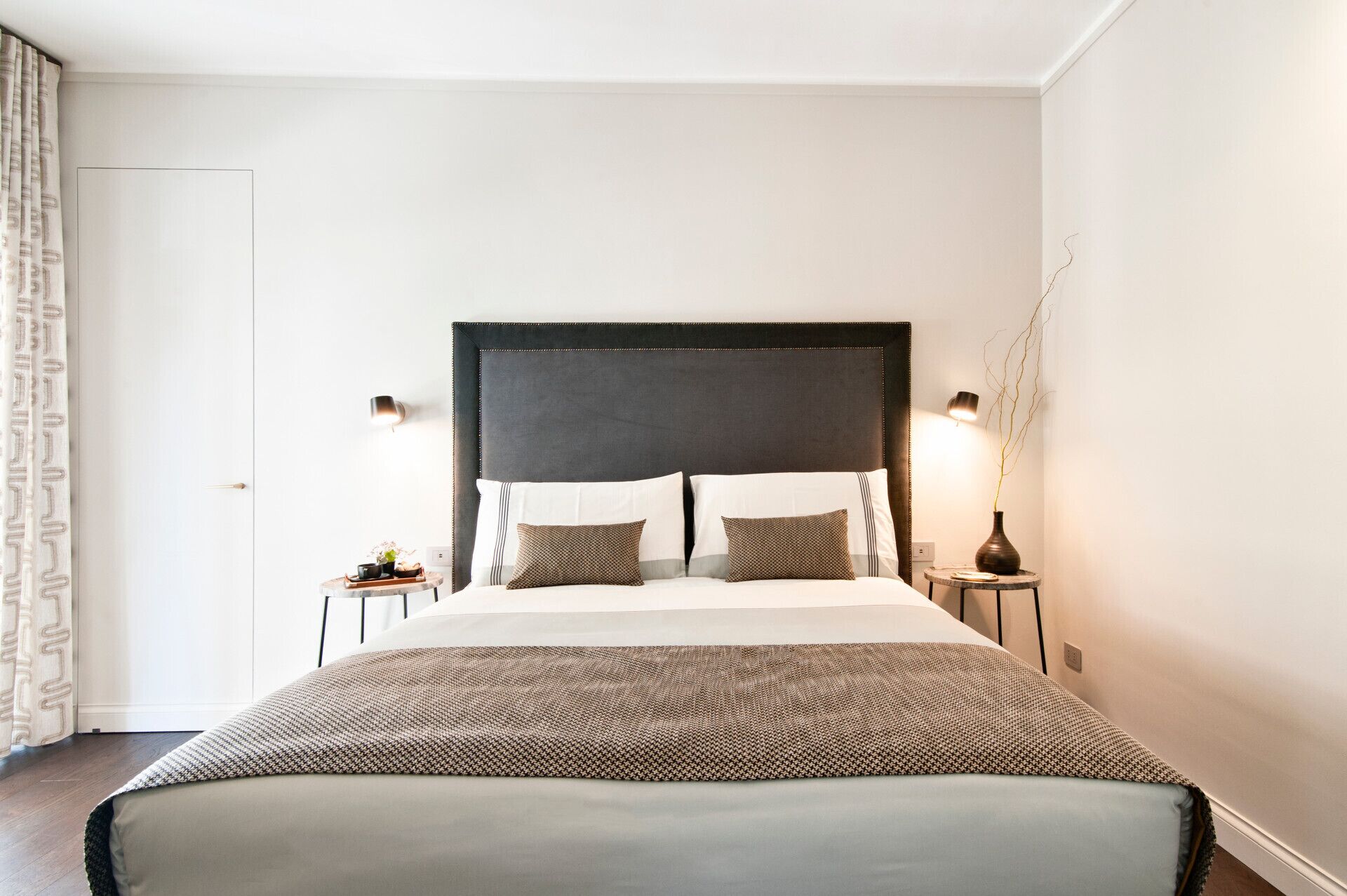 Quarto de hotel bem arrumado, com uma cama grande, duas mesas de cabeceira e uma luminária na parede.