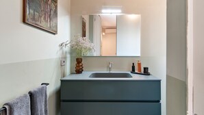A bathroom with a grey vanity, a mirror, a vase with flowers, and a towel rack. - HON Lecce Hospitality - Lecce Selection (Lecce)