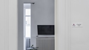 A minimalist living room with a white wall, a black flat-screen TV mounted above a white radiator, a small round table with a vase of flowers, and a chair. - InCentro Central Suite - Lecce Selection (Lecce)