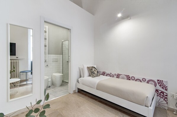 A modern bedroom with a white bed, a small bedside table, and a mirror.
