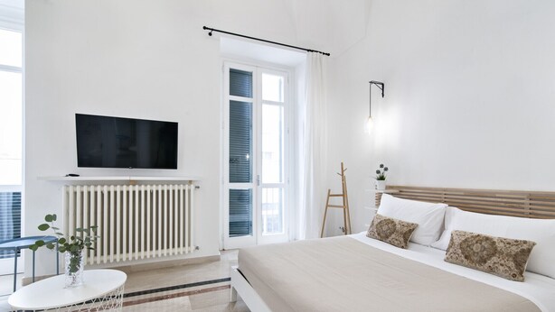 A modern bedroom with a bed, a TV, a radiator, and a window with curtains. - InCentro Central Suite - Lecce Selection (Lecce)