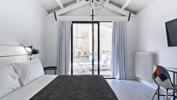 A bedroom with a bed, a desk, a chair, a radiator, and a view of an outdoor patio. - InCentro Exclusive Terrace Suite - Lecce Selection (Lecce)