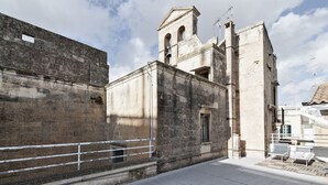 A courtyard with a stone wall, a bell tower, and a small balcony with a chair. - InCentro Exclusive Terrace Suite - Lecce Selection (Lecce)
