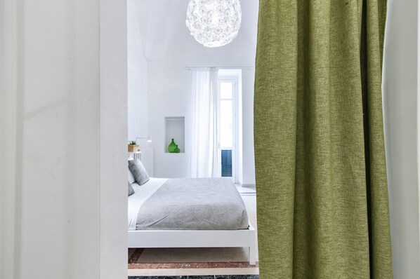 Une chambre moderne avec un lit, un radiateur blanc, un vase vert et une fenêtre avec des rideaux.