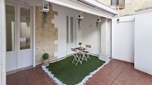A small patio with a table and chairs, a potted plant, and hanging plants.