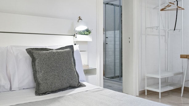 A bedroom with a bed, a bedside lamp, a hanging plant, a closet with a hanging rack, and a glass shower door.