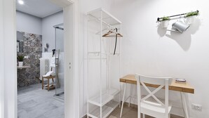A modern bathroom with a shower, a white chair, a wooden desk, and a hanging plant.
