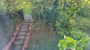 Una scala con ringhiera metallica, immersa nel verde e addossata a un muro di mattoni.