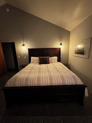 Un dormitorio con una cama grande, dos lámparas de noche, un cuadro enmarcado en la pared y una puerta al fondo.