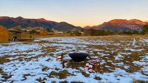 A snowy field with a fire pit and blankets, surrounded by mountains and a building. - Casa de Los sueños del mañana (El Prado)