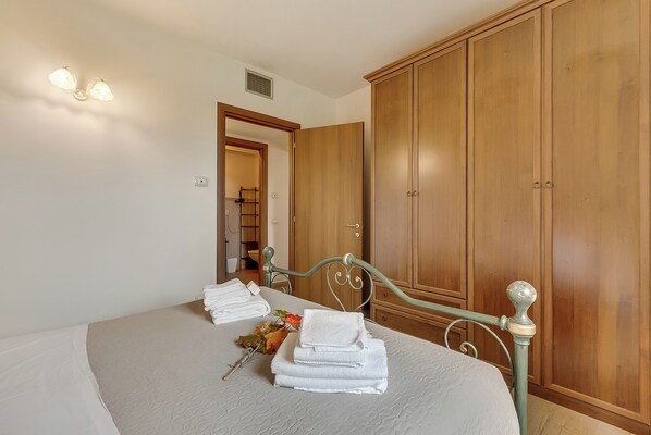 A neatly made bed with folded towels, a wooden wardrobe, and a bathroom visible in the background.