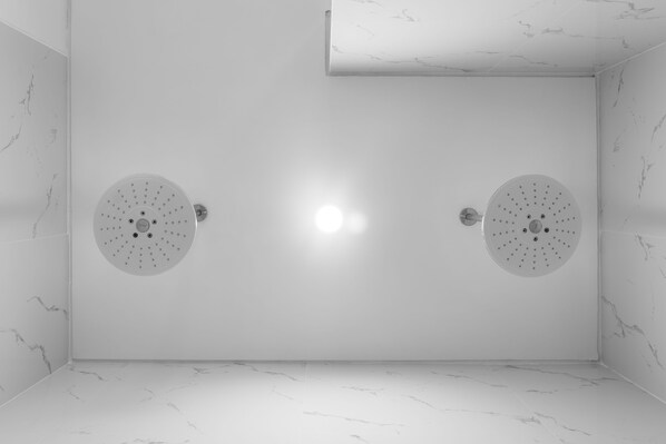 Un baño moderno con dos cabezales de ducha, paredes de mármol y un diseño limpio y minimalista.