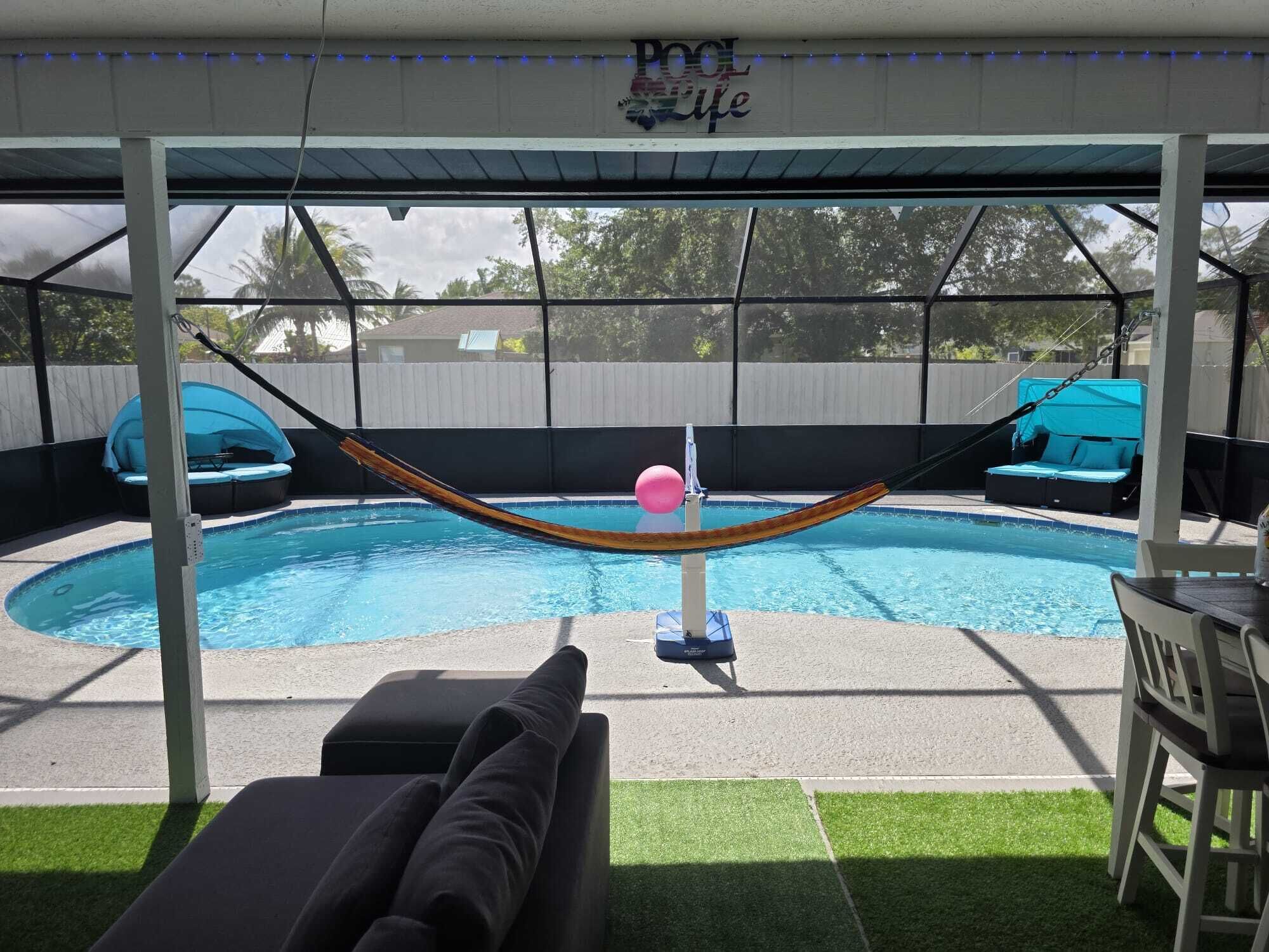 A covered outdoor pool area with a hammock, lounge chairs, and a table.