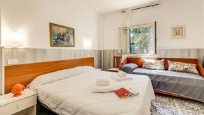 Habitación de hotel con una cama grande, una cama más pequeña, un escritorio, una silla, una ventana con cortinas y un cuadro en la pared.