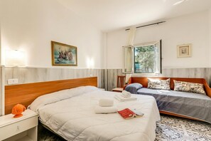 A hotel room with a large bed, a smaller bed, a desk, a chair, a window with curtains, and a painting on the wall. - Stella Marina Apartment 8, Vieste, Italy (Vieste)