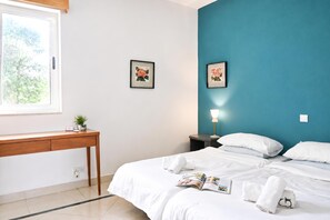 A hotel room with a bed, a bedside table, a desk, and two framed pictures on the wall.