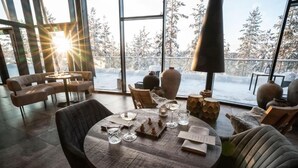 Un comedor acogedor con mesas y sillas redondas, ventanas amplias con vista a la nieve y una cálida lámpara colgante.