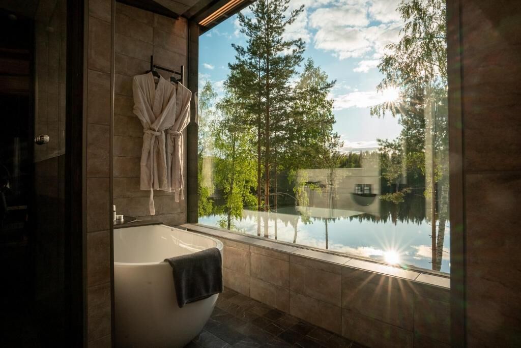 Un baño moderno con una bañera independiente, cabina de ducha con mampara de vidrio y vistas a un lago y árboles.
