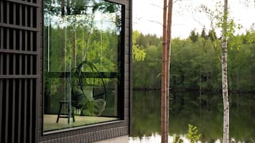 Eine Holzhütte mit großem Fenster mit Blick auf einen stillen See und dichten Wald.