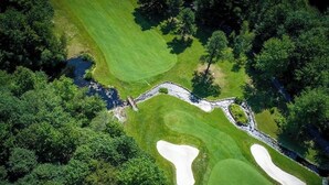 An aerial view of a golf course with sand bunkers, a water hazard, and dense trees. - Peaceful Two-Story Lake Naomi Home, Modern Design in Timber Trails + Lake Access (Pocono Pines)