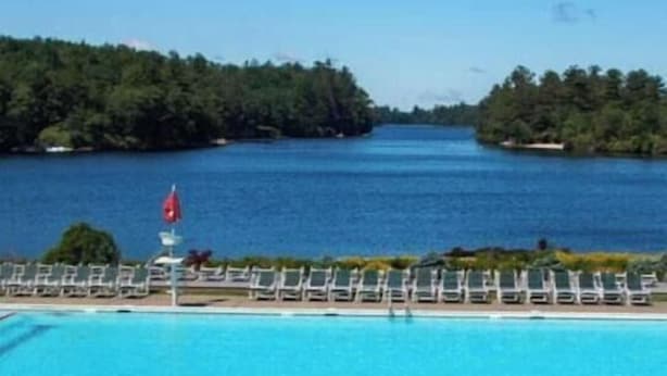 A swimming pool with clear blue water, surrounded by a white pool deck and a row of lounge chairs. - Peaceful Two-Story Lake Naomi Home, Modern Design in Timber Trails + Lake Access (Pocono Pines)